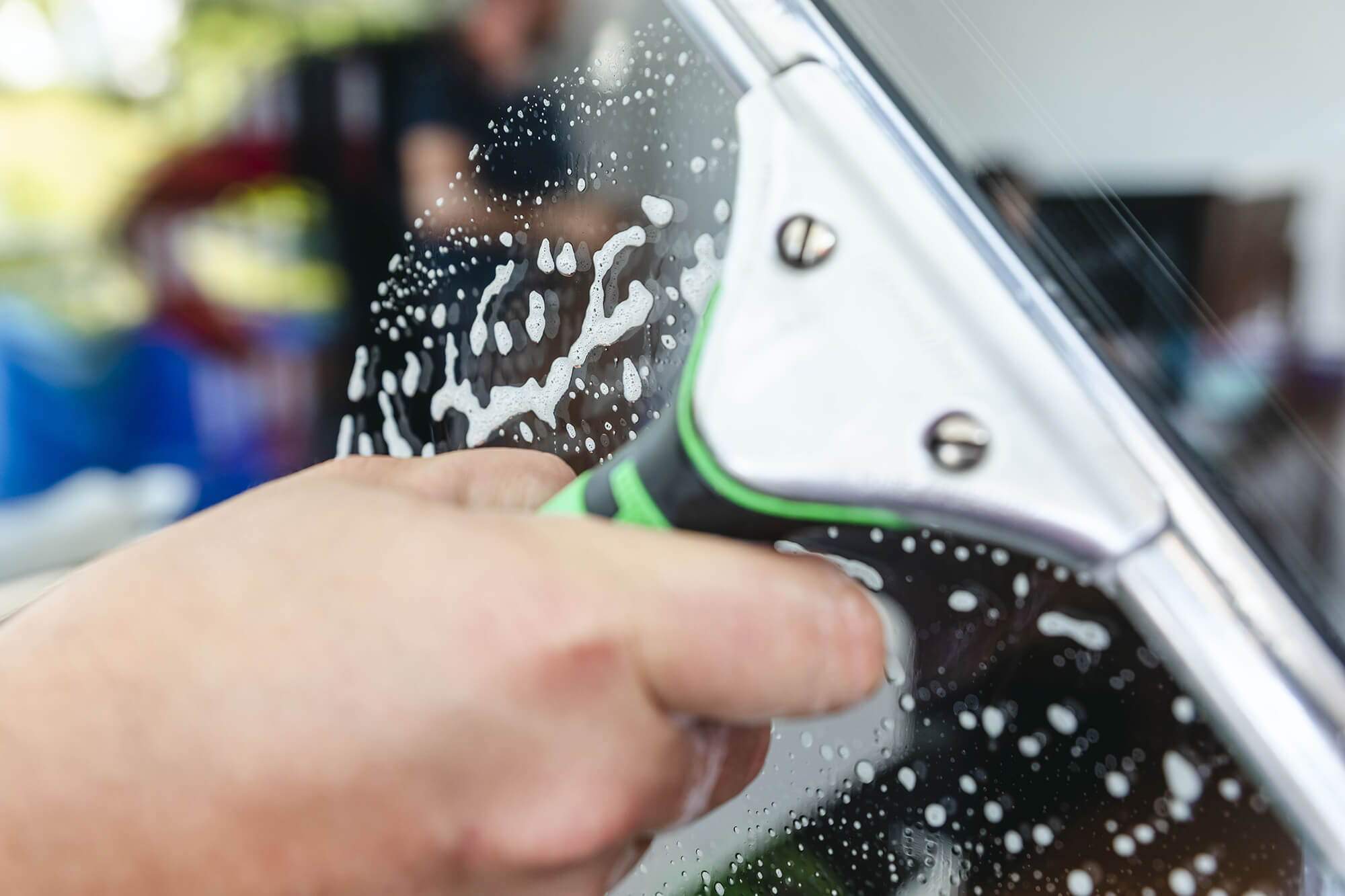 Nahaufnahme einer Hand, die mit einem Abzieher Seifenwasser von einer Glasscheibe entfernt – professionelle Fensterreinigung mit klarem Ergebnis.